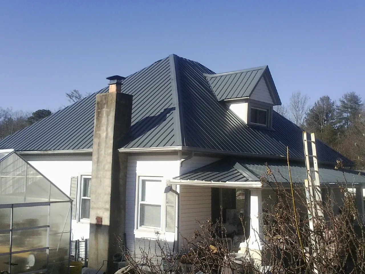 Dark blue standing seam metal roof on a white farmhouse with dormer — Slate & Tile Roof Repair by Roofing Brothers in Jasper