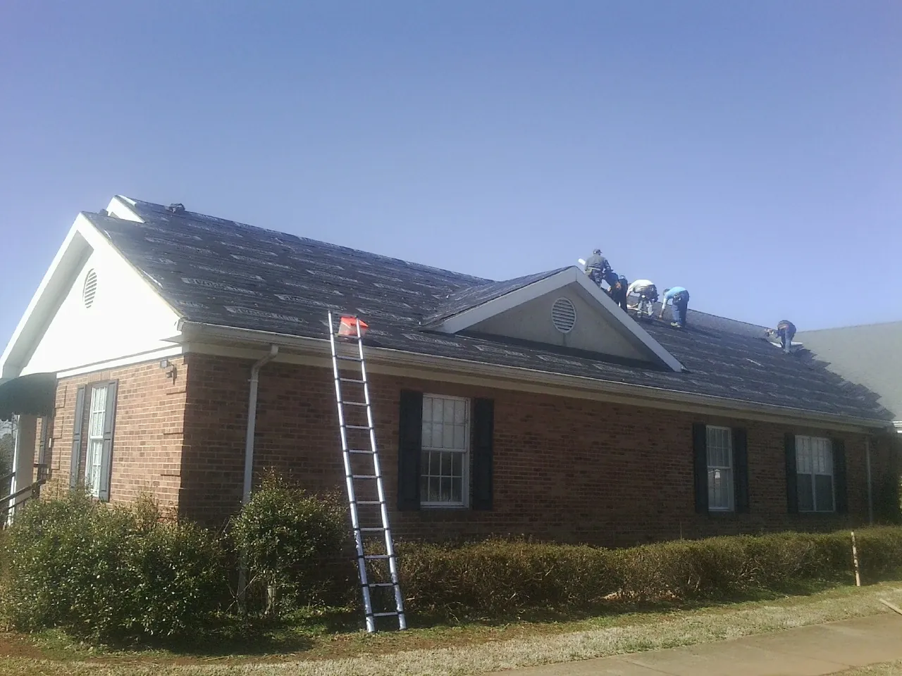 Crew tearing shingles off a brick ranch roof with a ladder set — Metal Roof Repair work by our crew in Jasper
